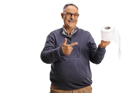 Téléchargez les photos : Homme mûr souriant tenant un rouleau de papier toilette et pointant isolé sur fond blanc - en image libre de droit
