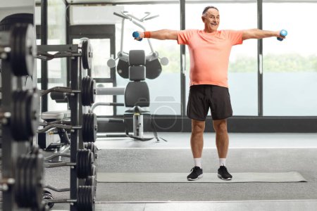 Téléchargez les photos : Portrait complet d'un homme mature faisant de l'exercice avec de petits poids dans une salle de gym - en image libre de droit