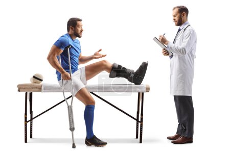 Téléchargez les photos : Joueur de football avec une blessure à la jambe parler à un médecin masculin isolé sur fond blanc - en image libre de droit