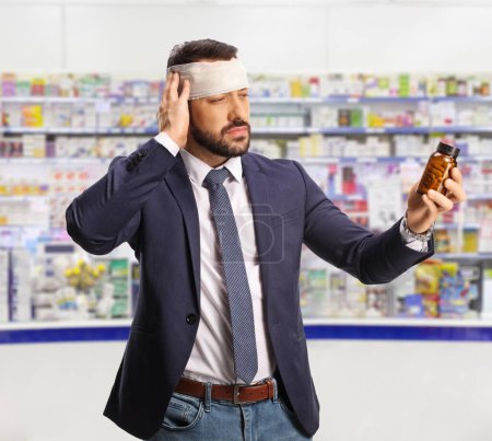 Téléchargez les photos : Homme avec une tête blessée tenant une bouteille d'analgésique à la pharmacie - en image libre de droit