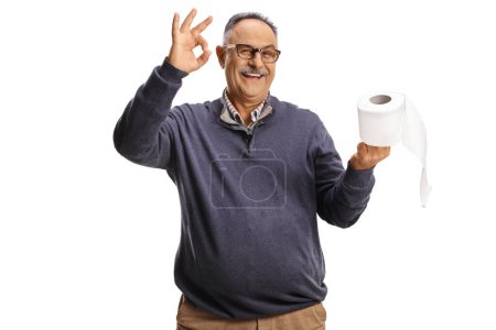 Photo for Smiling mature man holding a toilet paper roll and gesturing ok sign isolated on white background - Royalty Free Image