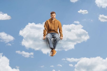 Téléchargez les photos : Un type en jean et un sweat à capuche assis sur un nuage dans le ciel - en image libre de droit