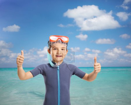 Foto de Niño sonriente con una máscara de snorkel mostrando los pulgares junto al mar - Imagen libre de derechos