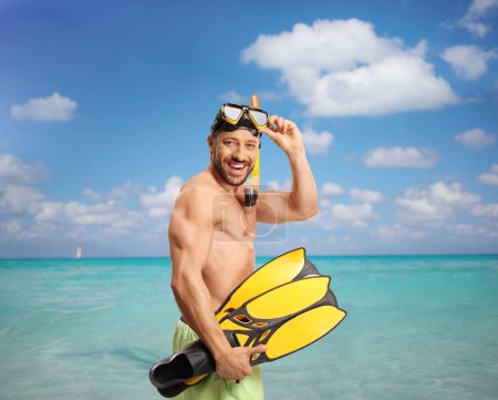 Photo for Cheerful young man in swimwear with a diving mask and snorkeling fins in the sea smiling at camera - Royalty Free Image