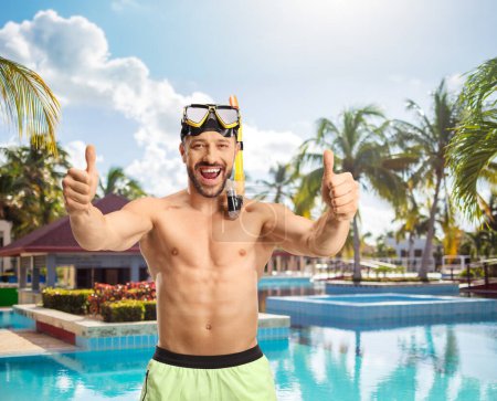 Photo for Cheerful man in a swimsuit with a diving mask showing thumbs up in front of a swimming pool - Royalty Free Image