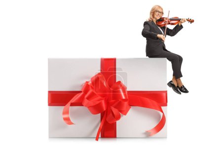 Téléchargez les photos : Femme assise sur une boîte cadeau et jouant un violon isolé sur fond blanc - en image libre de droit