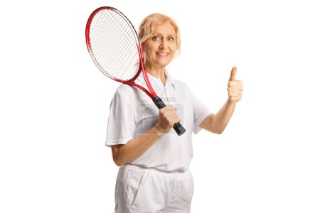 Téléchargez les photos : Femme d'âge moyen tenant une raquette de tennis sur son épaule et les pouces geste vers le haut solitaire sur fond blanc - en image libre de droit