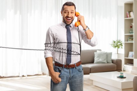 Photo for Man tied with a rotary phone cable at home, having a conversation and smiling - Royalty Free Image