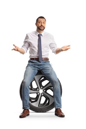 Téléchargez les photos : Sérieux jeune homme assis sur un pneu de voiture isolé sur fond blanc - en image libre de droit