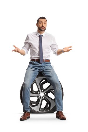 Téléchargez les photos : Homme malheureux assis sur un pneu de voiture à plat isolé sur fond blanc - en image libre de droit