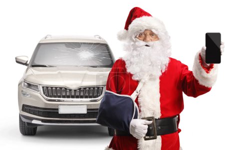 Téléchargez les photos : Père Noël avec un bras blessé d'une blessure d'accident de voiture tenant un smartphone isolé sur fond blanc - en image libre de droit