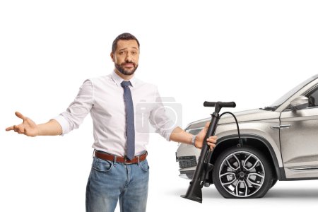 Photo for Irritated young man holding a manual tire pump in front of a car with flat tire - Royalty Free Image