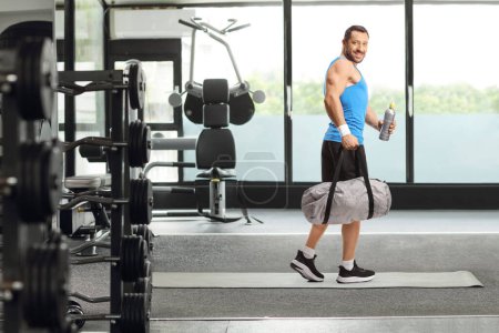 Foto de Hombre con una bolsa de deporte caminando en un gimnasio y sosteniendo una botella - Imagen libre de derechos