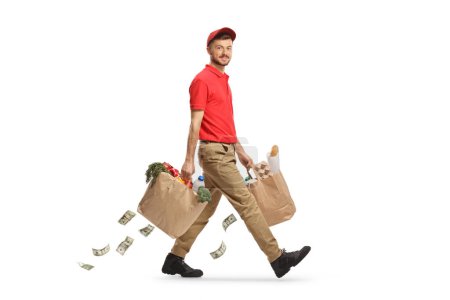 Foto de Largura completa de un repartidor llevando bolsas de comestibles y dinero cayendo aislado sobre fondo blanco - Imagen libre de derechos
