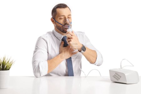 Photo for Young man sitting at a table and using a nebulizer isolated on white backgroun - Royalty Free Image