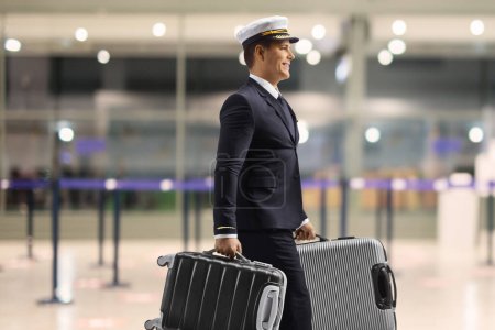 Photo for Profile shot of a pilot walking in an airport hall and carrying suitcases - Royalty Free Image