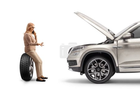 Téléchargez les photos : Femme avec un problème de voiture assis sur un pneu et faire un appel téléphonique isolé sur fond blanc - en image libre de droit