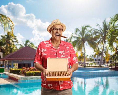 Photo for Cheerful man holding a wooden box of cigars and smiling by a swimming pool - Royalty Free Image