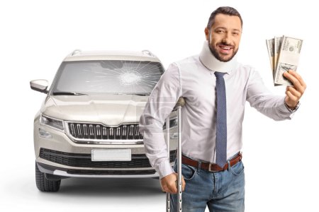 Photo for Injured man in a car crasg with a cervical collar leaning on crutches and holding stacks of money isolated on white background - Royalty Free Image