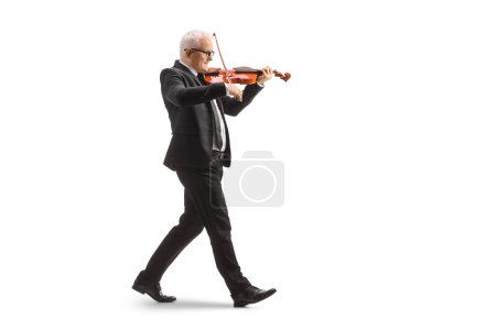 Photo for Full length profile shot of a man in a black suit walking and playing a violin isolated on white background - Royalty Free Image