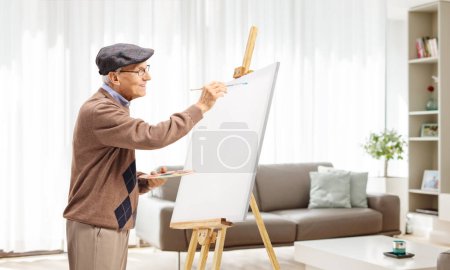 Téléchargez les photos : Homme âgé peignant sur une toile dans un salon - en image libre de droit