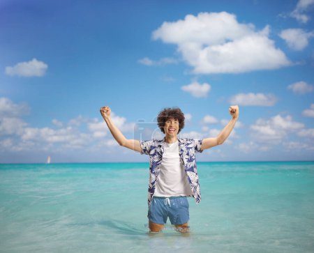 Photo for Overjoyed young man on a summer holiday gesturing happiness with arms up in the sea - Royalty Free Image