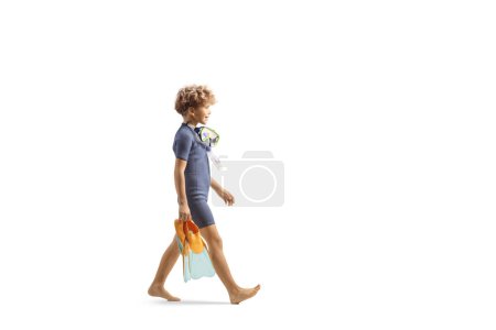 Photo for Full length profile shot of boy wearing a diving suit, carrying a mask and fins and walking isolated on white background - Royalty Free Image