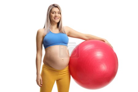 Téléchargez les photos : Femme enceinte avec un haut de culture et des leggings tenant une balle de fitness isolée sur fond blanc - en image libre de droit