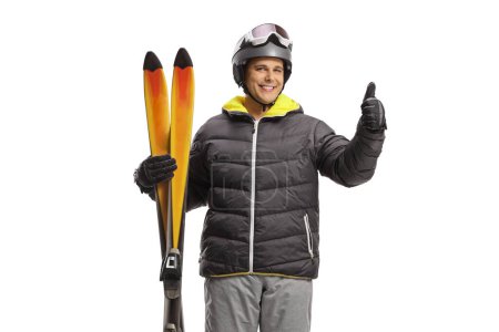 Foto de Joven sosteniendo un par de esquís y señalando un cartel con el pulgar hacia arriba aislado sobre un fondo blanco - Imagen libre de derechos