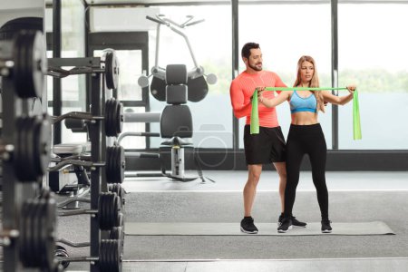 Foto de Entrenador de fitness masculino mostrando un ejercicio a una mujer con una banda elástica en el gimnasio - Imagen libre de derechos