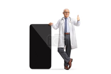Photo for Male doctor leaning on a smartphone and gesturing thumbs up isolated on white background - Royalty Free Image