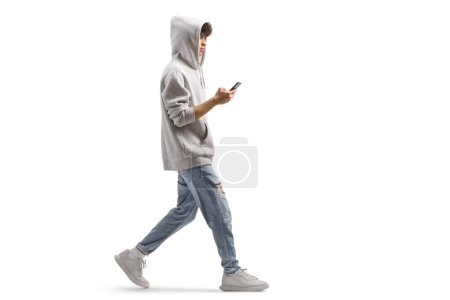 Téléchargez les photos : Plan complet d'un gars portant un sweat à capuche gris et marchant avec un smartphone isolé sur fond blanc - en image libre de droit