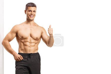 Foto de Hombre musculoso apoyado sin camisa en una pared y mostrando los pulgares hacia arriba aislado sobre fondo blanco - Imagen libre de derechos