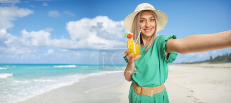 Foto de Mujer joven con una copa de cóctel tomando una selfie en una playa - Imagen libre de derechos