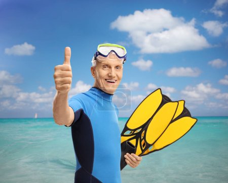 Foto de Hombre mayor con equipo de snorkel haciendo una señal de pulgar hacia arriba junto al mar - Imagen libre de derechos