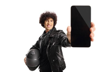 Téléchargez les photos : Biker dans une veste en cuir noir tenant un casque et un smartphone isolé sur fond blanc - en image libre de droit