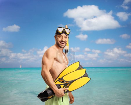 Foto de Joven en traje de baño con una máscara de buceo sosteniendo aletas junto al mar - Imagen libre de derechos