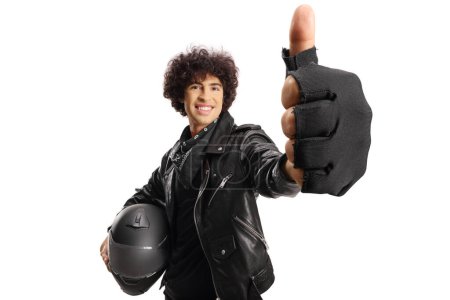 Photo for Handsome guy in a black leather jacket holding a helmet and gesturing thumbs up isolated on white background - Royalty Free Image