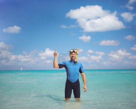 Téléchargez les photos : Jeune homme portant une combinaison et un masque de plongée et pointant vers le haut dans la mer - en image libre de droit