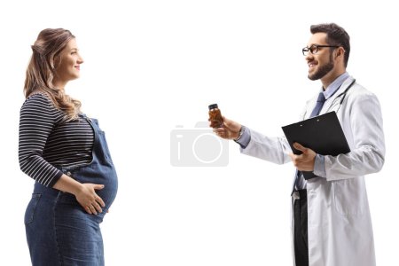 Téléchargez les photos : Plan du profil d'un médecin donnant une bouteille de pilules vitaminiques à une femme enceinte isolée sur fond blanc - en image libre de droit