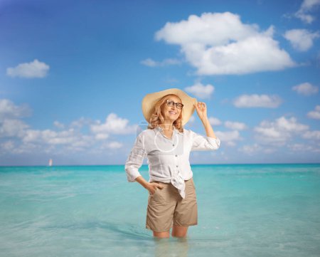 Téléchargez les photos : Femme d'âge moyen avec un chapeau de paille posant dans la mer - en image libre de droit