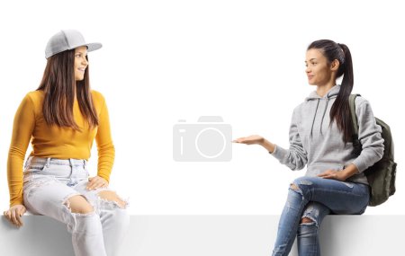 Photo for Female friends sitting on a blank panel and having a conversation isolated on white background - Royalty Free Image
