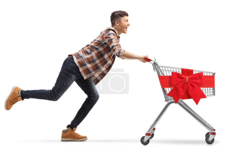 Photo for Young man running with an empty shopping cart tied with a red bow isolated on white background - Royalty Free Image