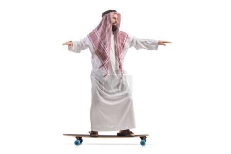Téléchargez les photos : Saoudien arabe en robe ethnique chevauchant un skateboard isolé sur fond blanc - en image libre de droit
