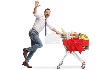 Foto de Hombre corriendo con comida en un carrito de la compra y saludando a la cámara aislado sobre fondo blanco - Imagen libre de derechos