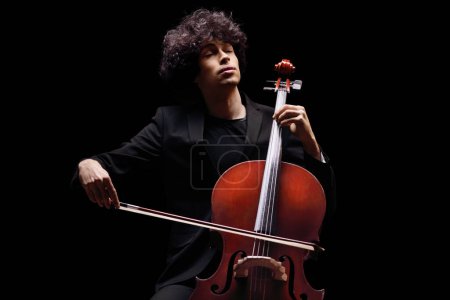 Téléchargez les photos : Jeune artiste masculin jouant un violoncelle isolé sur fond noir - en image libre de droit