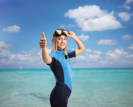 Foto de Mujer joven en el mar usando un traje de buceo y máscara y gestos pulgares hacia arriba - Imagen libre de derechos