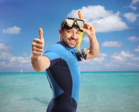 Téléchargez les photos : Jeune homme dans la mer vêtu d'une combinaison de plongée et d'un masque et levant les pouces - en image libre de droit