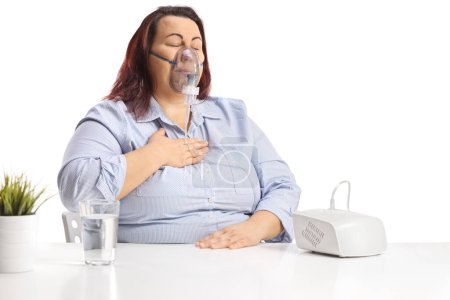 Téléchargez les photos : Plus size woman holding her chest and using a nebulizer isolated on white background - en image libre de droit