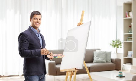 Photo for Young man painting on a canvas at home and smiling at camera - Royalty Free Image